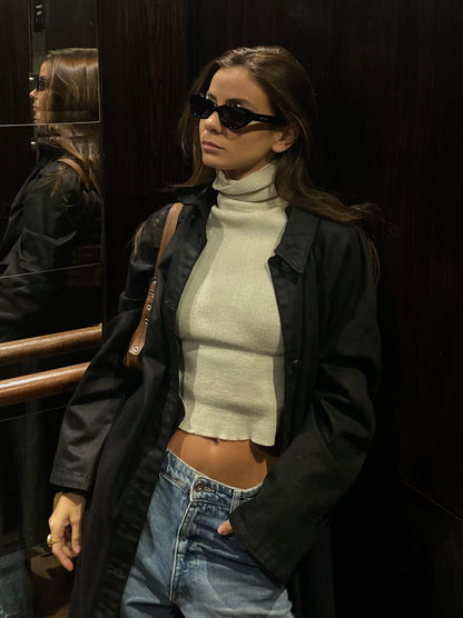 Woman wearing sunglasses, a black jacket, white turtleneck, and blue jeans in an elevator.
