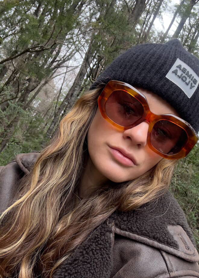 Person wearing a black beanie and brown sunglasses with a forest background