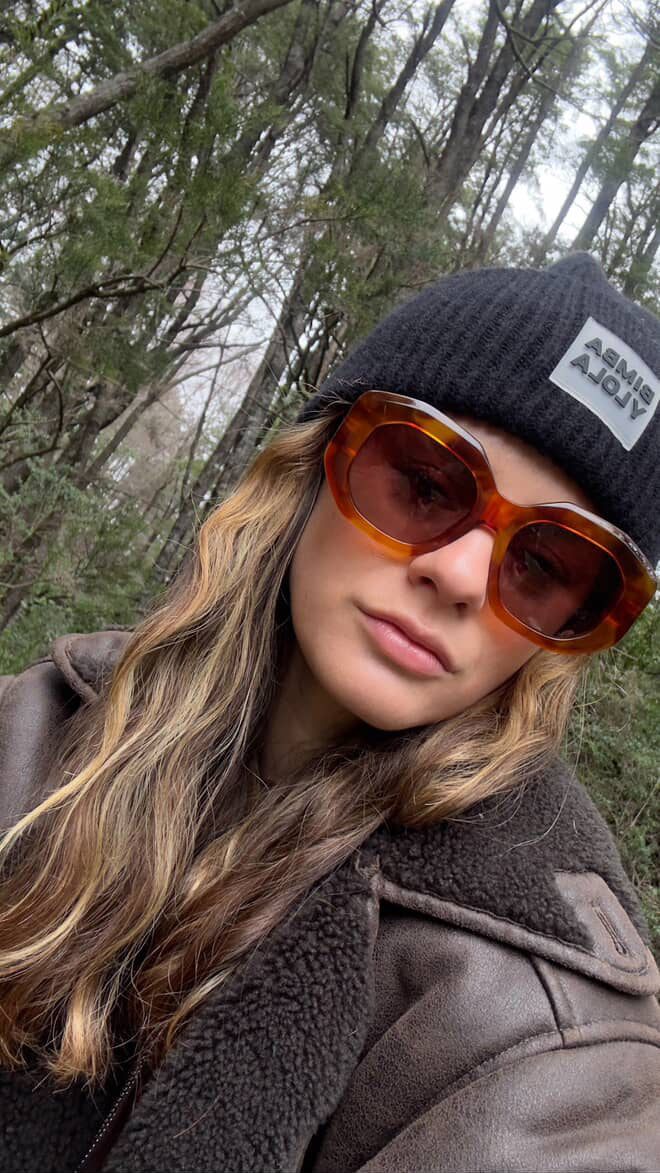 Person wearing a black beanie and brown sunglasses with a forest background