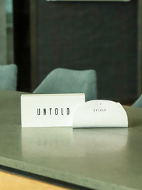 Thumbnail for UNTOLD branding on a card and packaging on a reflective surface with blurred background