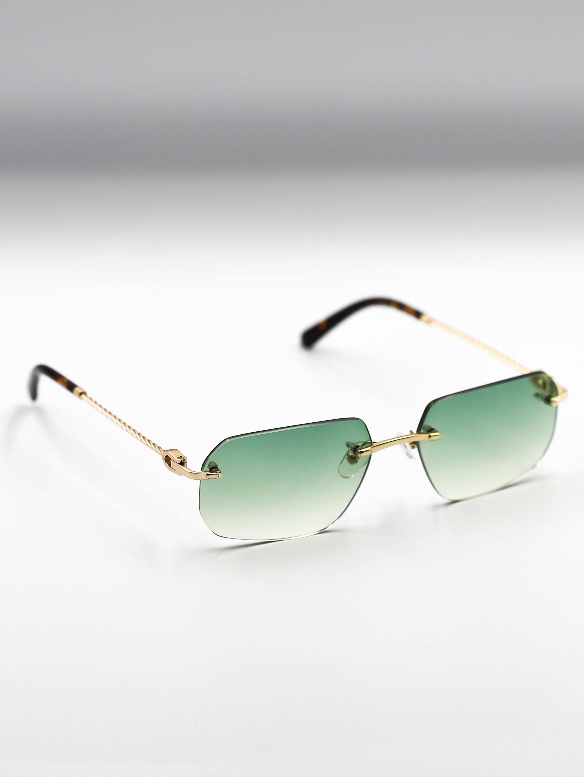Sunglasses with gold frame and green gradient lenses on a light gray background