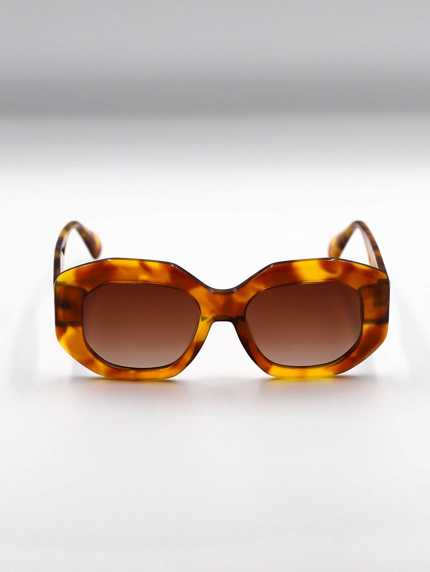 Sunglasses with tortoiseshell frame and brown lenses on a light gray background