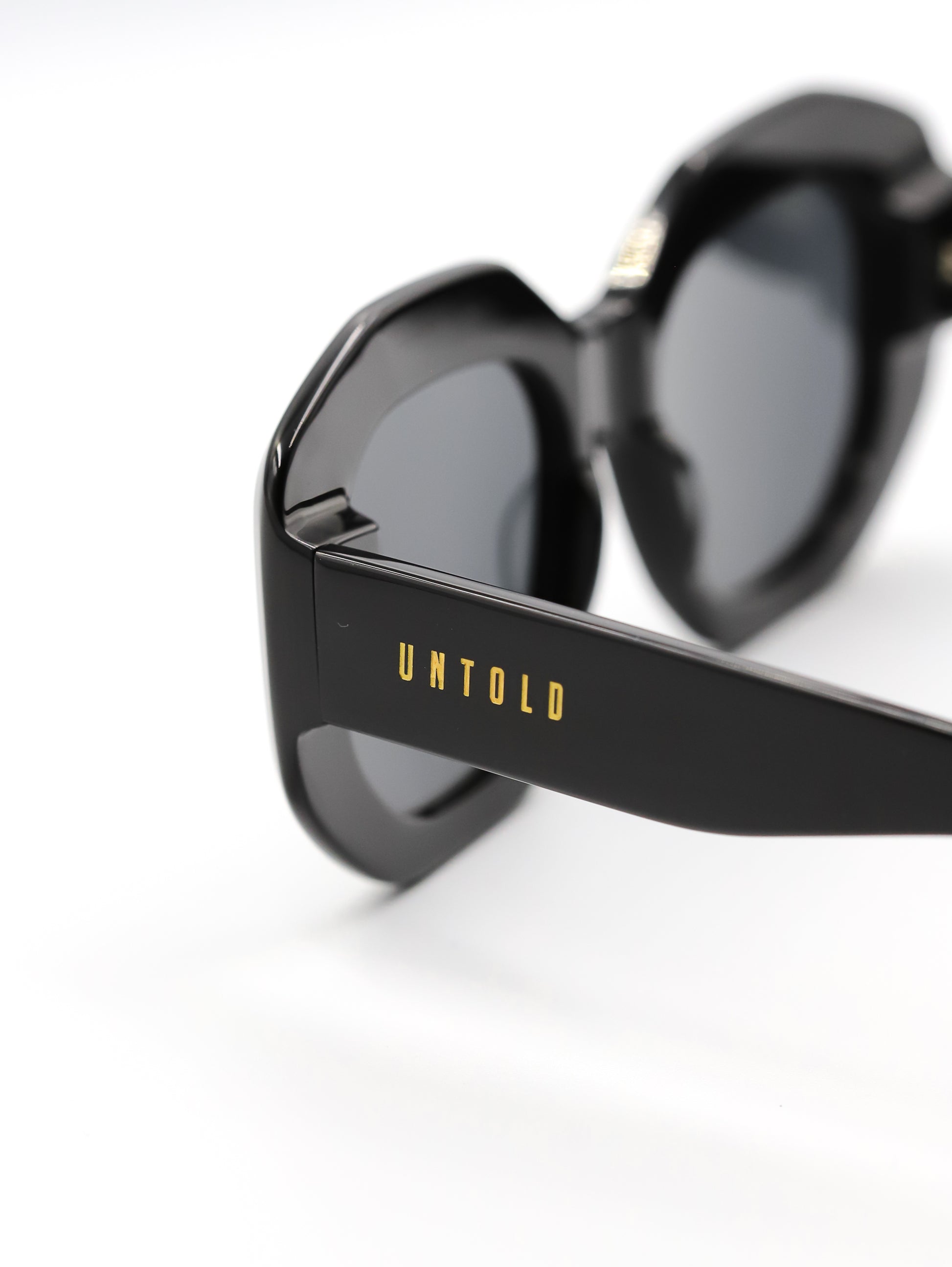 Black sunglasses with 'Untold' branding on a white background