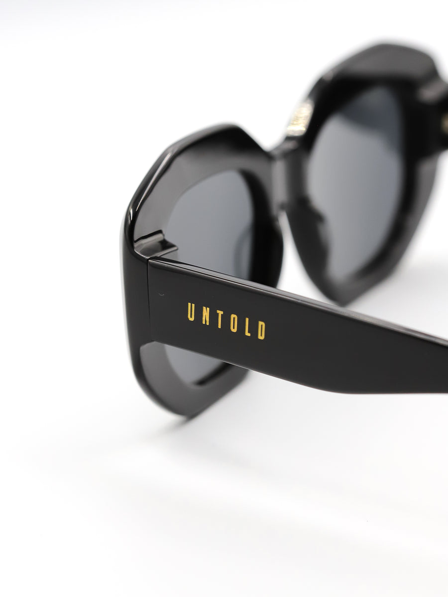 Black sunglasses with 'Untold' branding on a white background