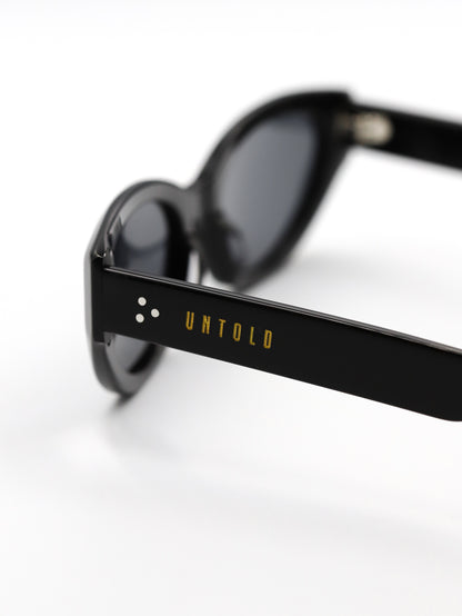 Black sunglasses with 'Untold' branding on a white background