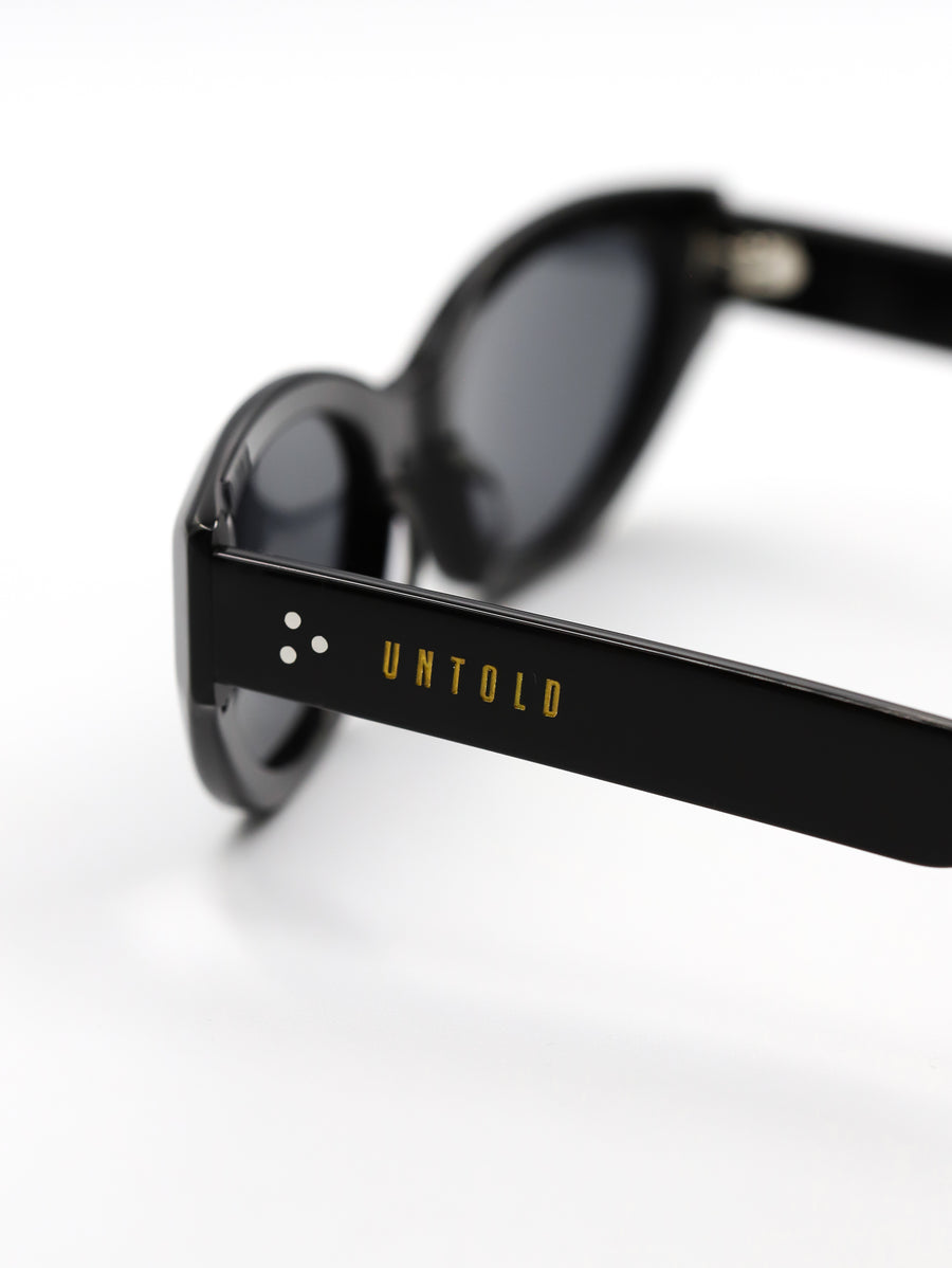 Black sunglasses with 'Untold' branding on a white background