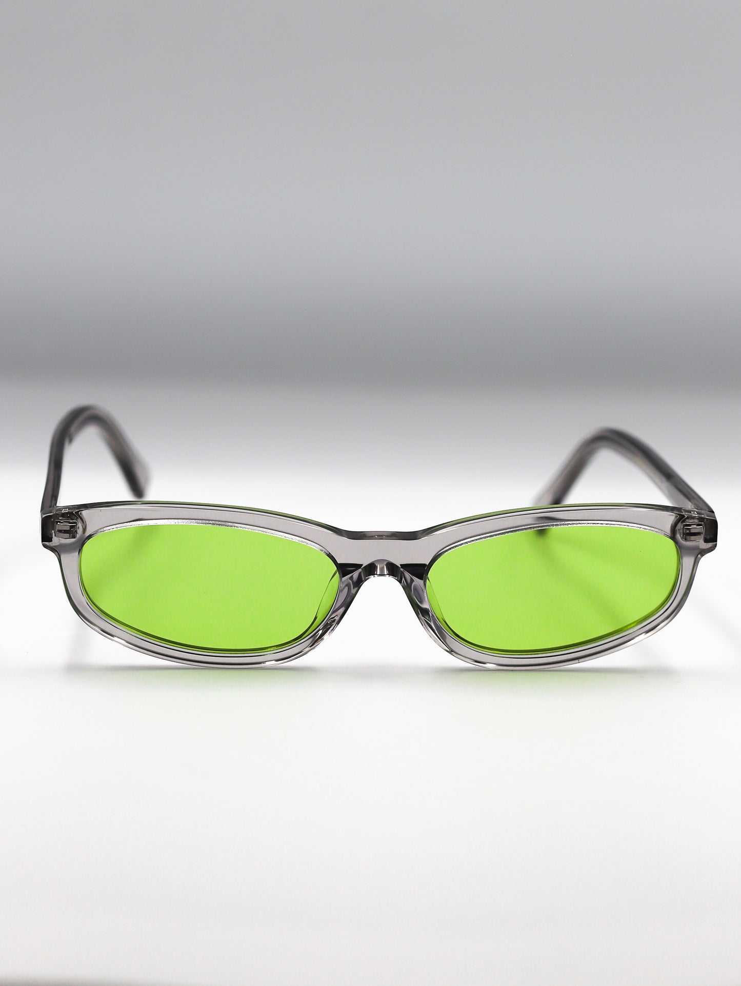 Sunglasses with green lenses and clear frames on a gradient gray background
