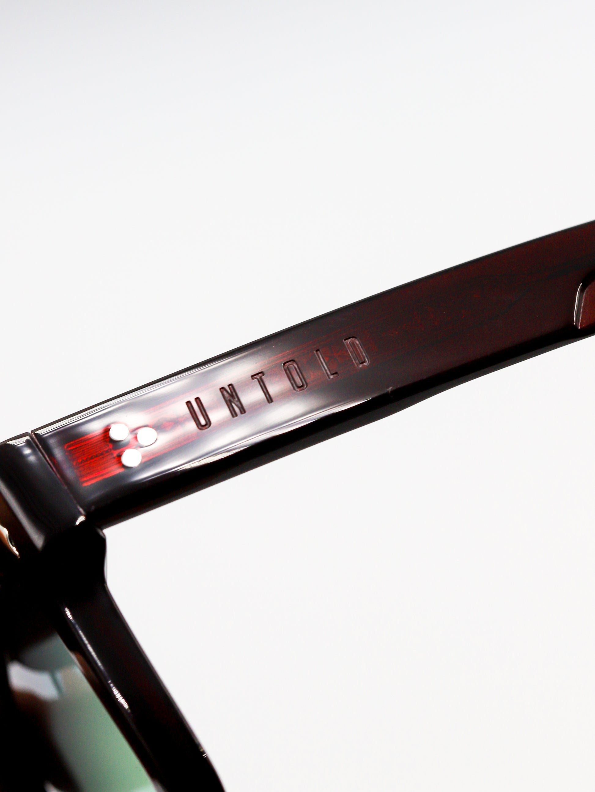 Close-up of a sunglasses frame with 'Untold' branding on a white background