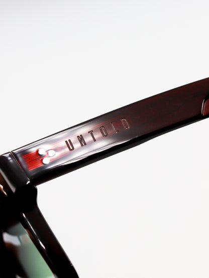Close-up of a sunglasses frame with 'Untold' branding on a white background