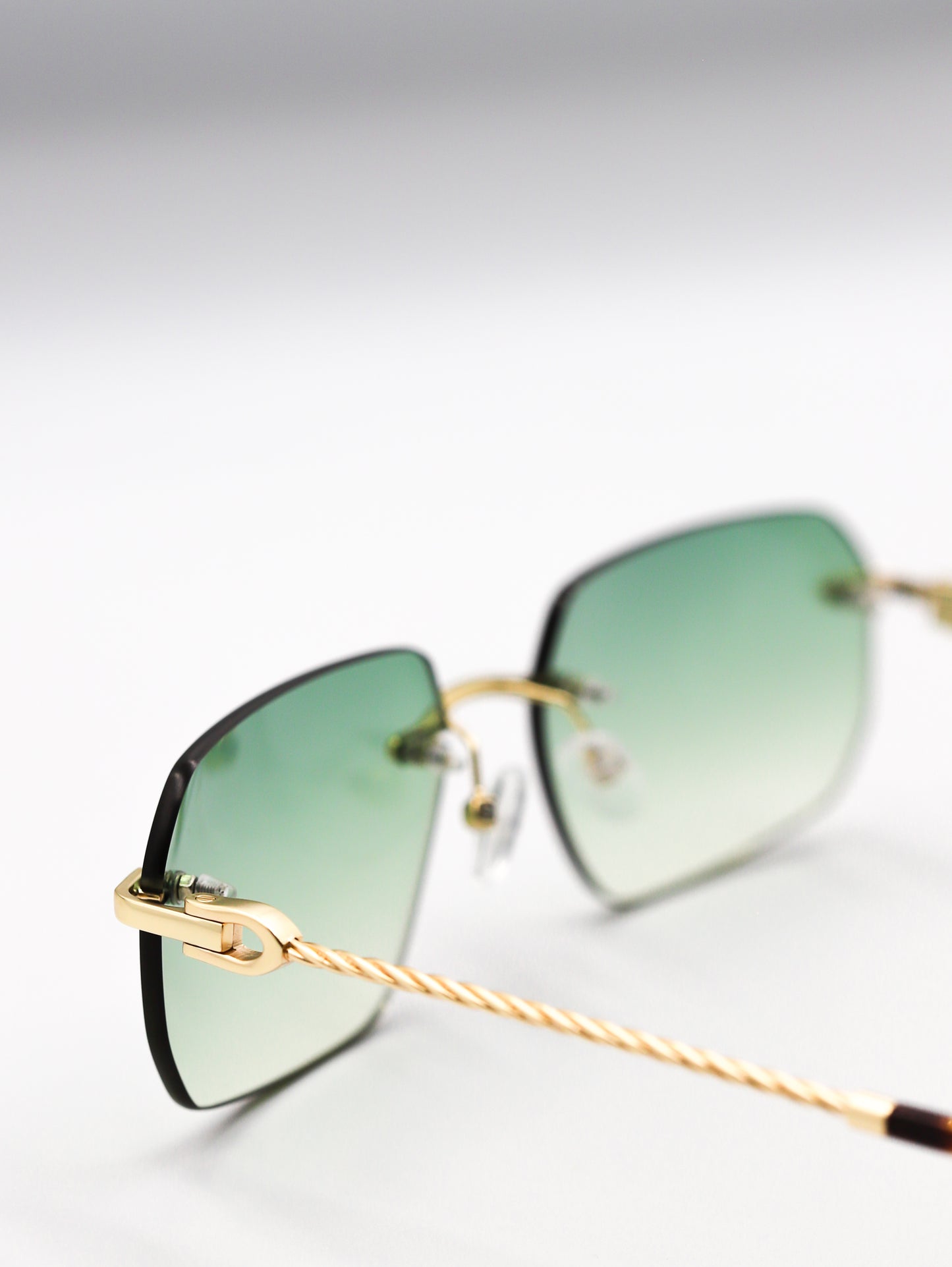 Sunglasses with gold frame and green lenses on a light gray background